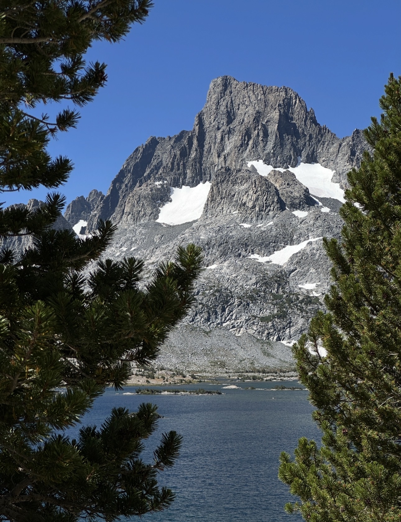 Banner Peak rising above an alpine lake framed by pine trees