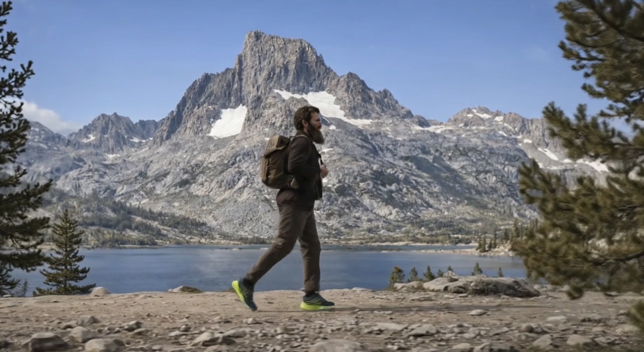 Hiker walking in front of Banner Peak and alpine lake, neon green shoes catching the light